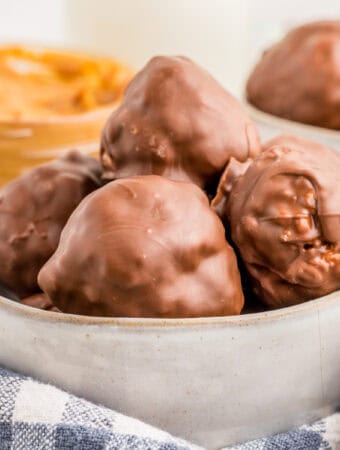 Square image of peanut butter balls in bowl with peanut butter in background.