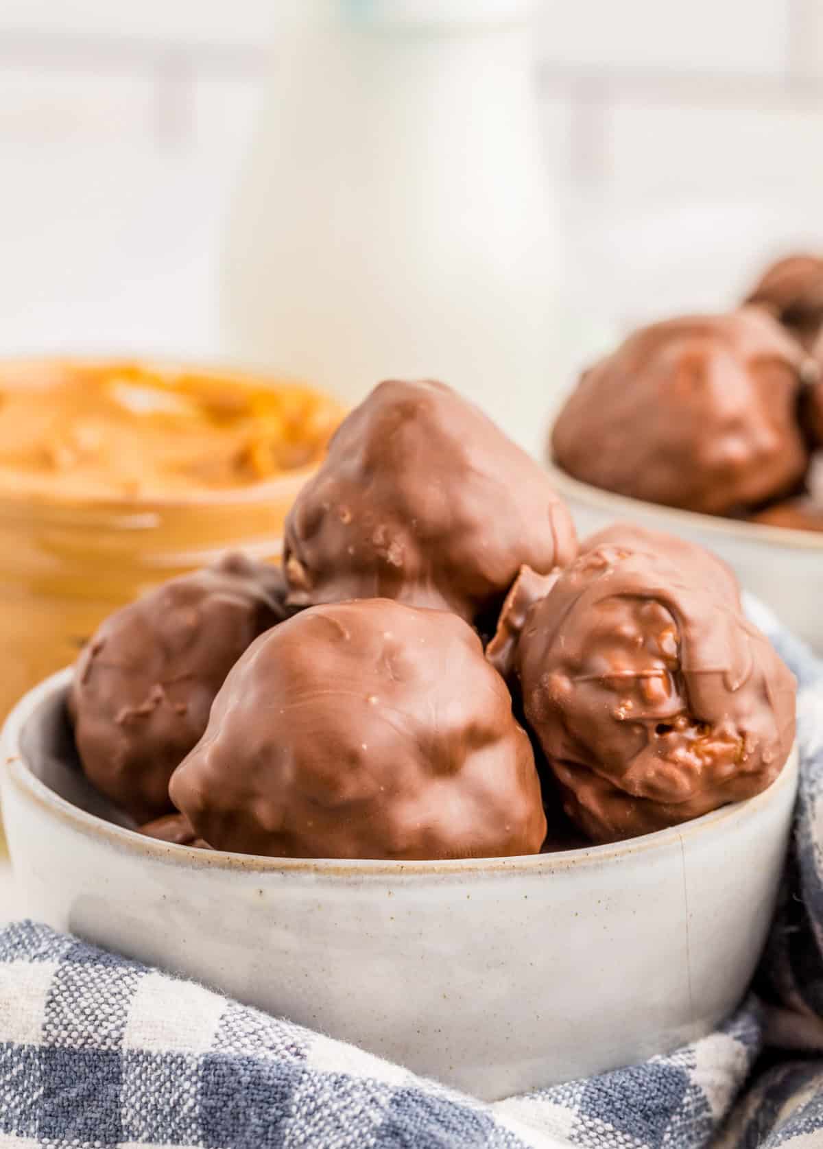 Stacked Rice Krispie Peanut Butter Balls stacked in bowl with peanut butter and milk in background.