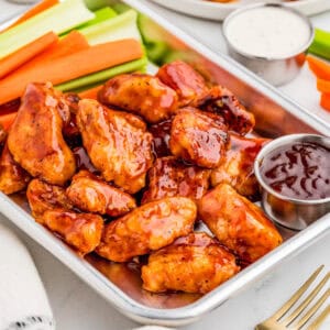 Close up square image of chicken on metal tray with vegetables and bbq sauce.