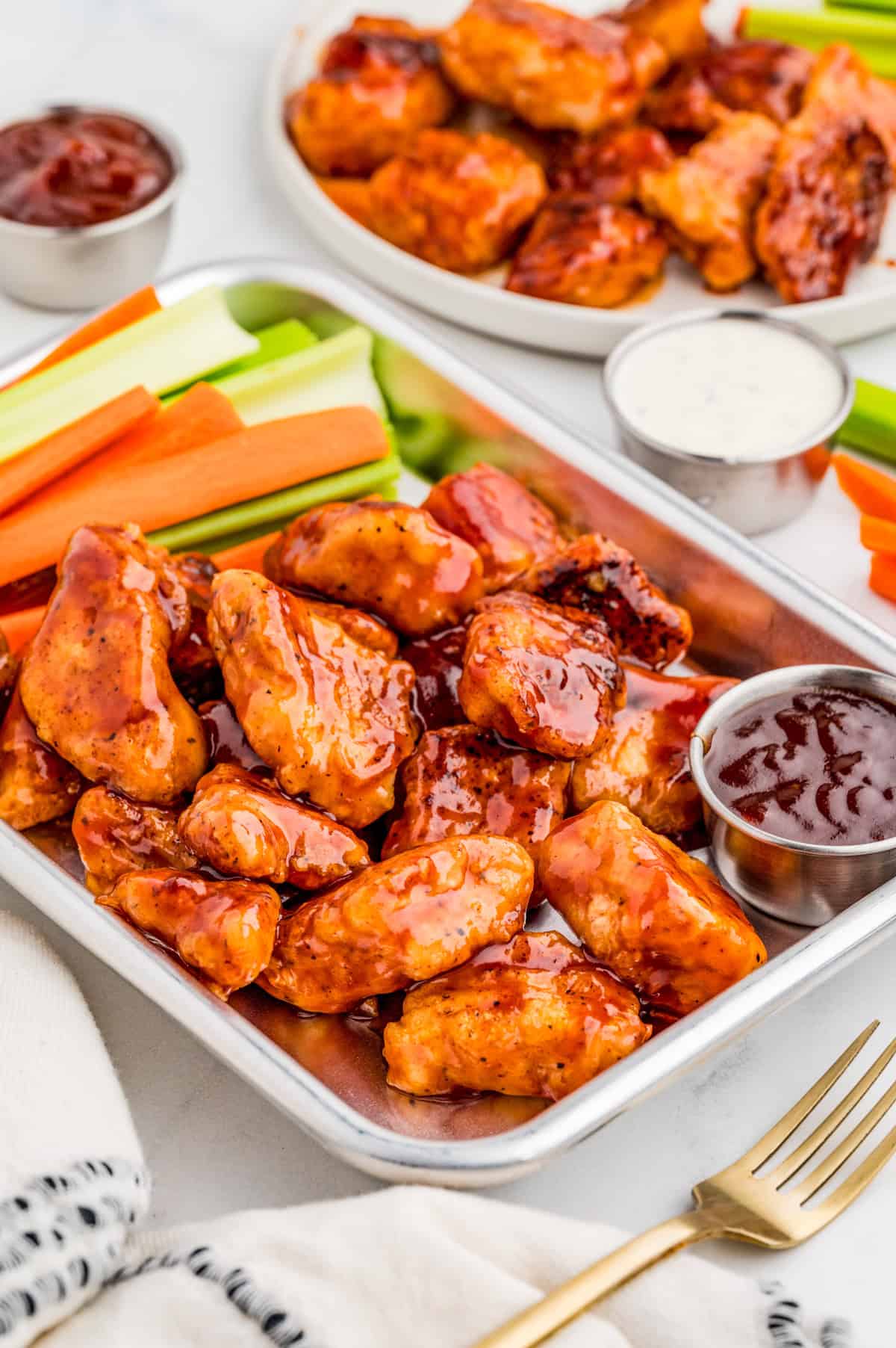 BBQ Chicken Bites on metal tray with vegetables and bbq sauce with more chicken and ranch in background.