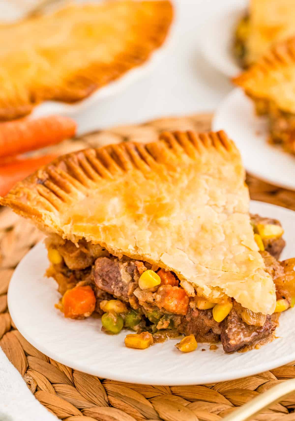 Slice of Beef Pot Pie on white plate on wicker mat.