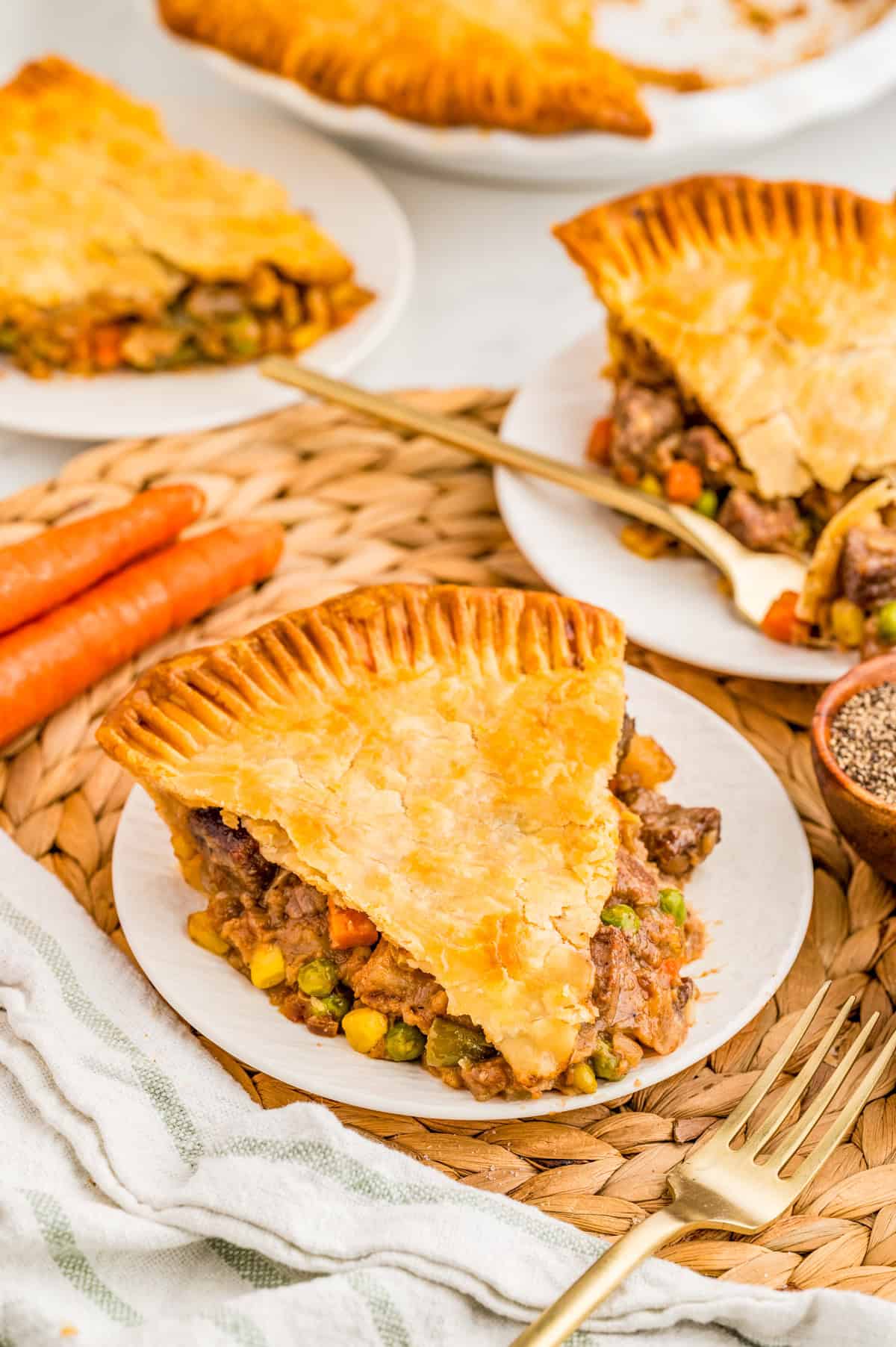 Slices of pie on white plates with carrots, linens and silverware.