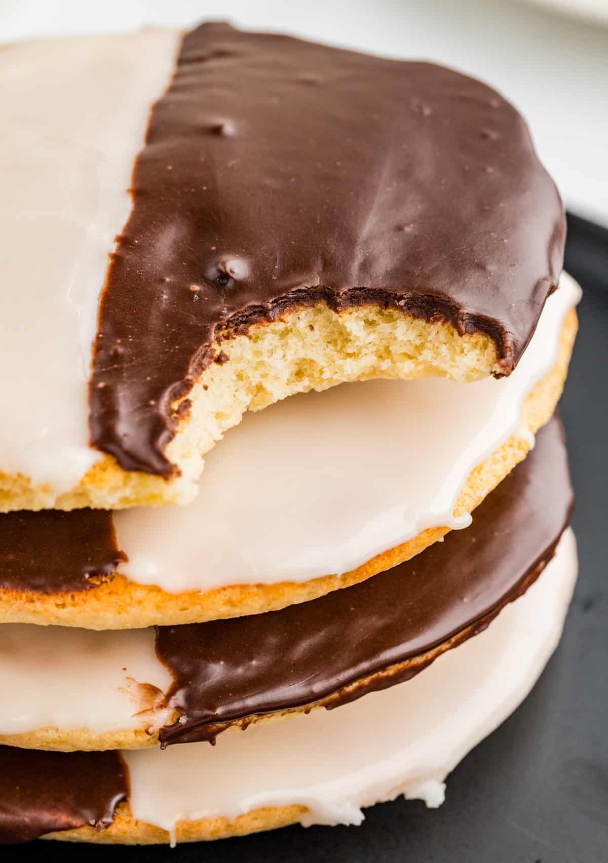 Stacked Black and White cookies on black plate with top cookie with a bite taken out of it.