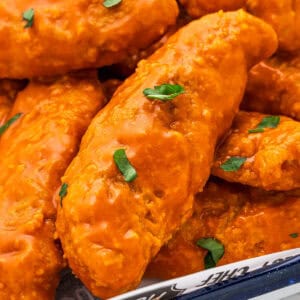 Close up square image of chicken strips layered on pan and topped with parsley.