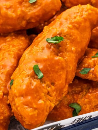 Close up square image of chicken strips layered on pan and topped with parsley.