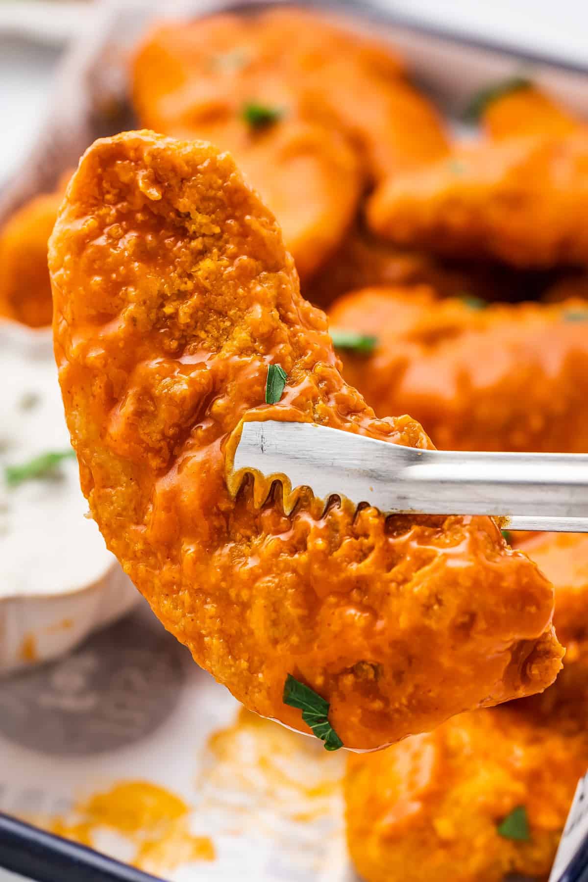 Tongs holding up one of the chicken strips off of the pan.