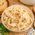 Square image of sauce over pasta in white bowl topped with parsley.
