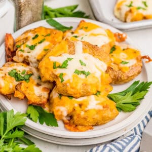 Square image of potatoes stacked on white plate topped with parsley.