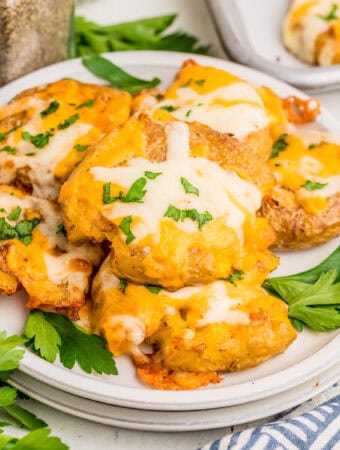 Square image of potatoes stacked on white plate topped with parsley.