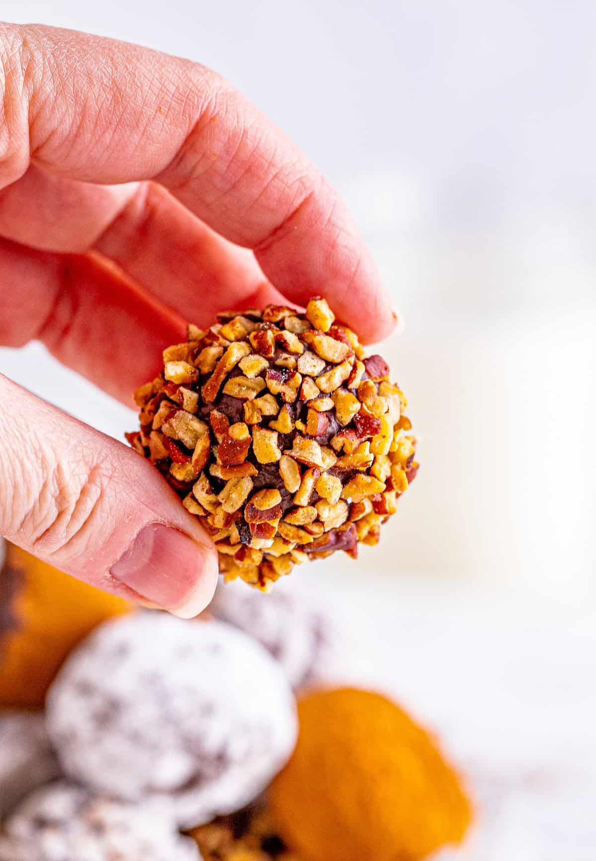 Hand holding one of the truffles that has been rolled in chopped nuts.