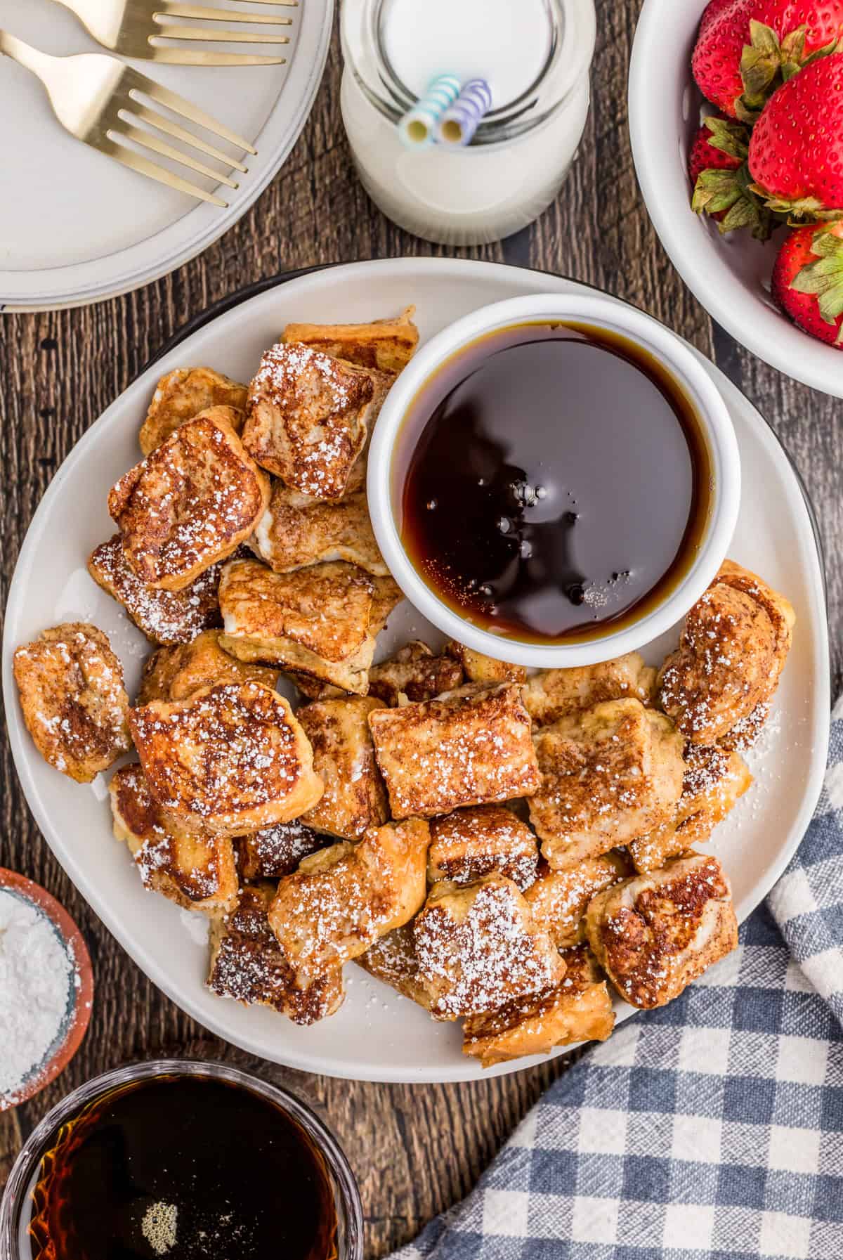 Overhead image of bites on white plate with bowl of syrup and coffee, milk strawberries around plate.