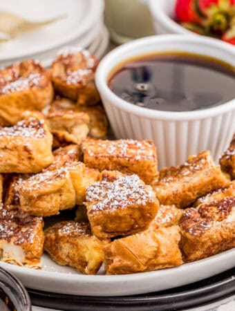 Close up square image of bites on white plate with bowl of syrup.