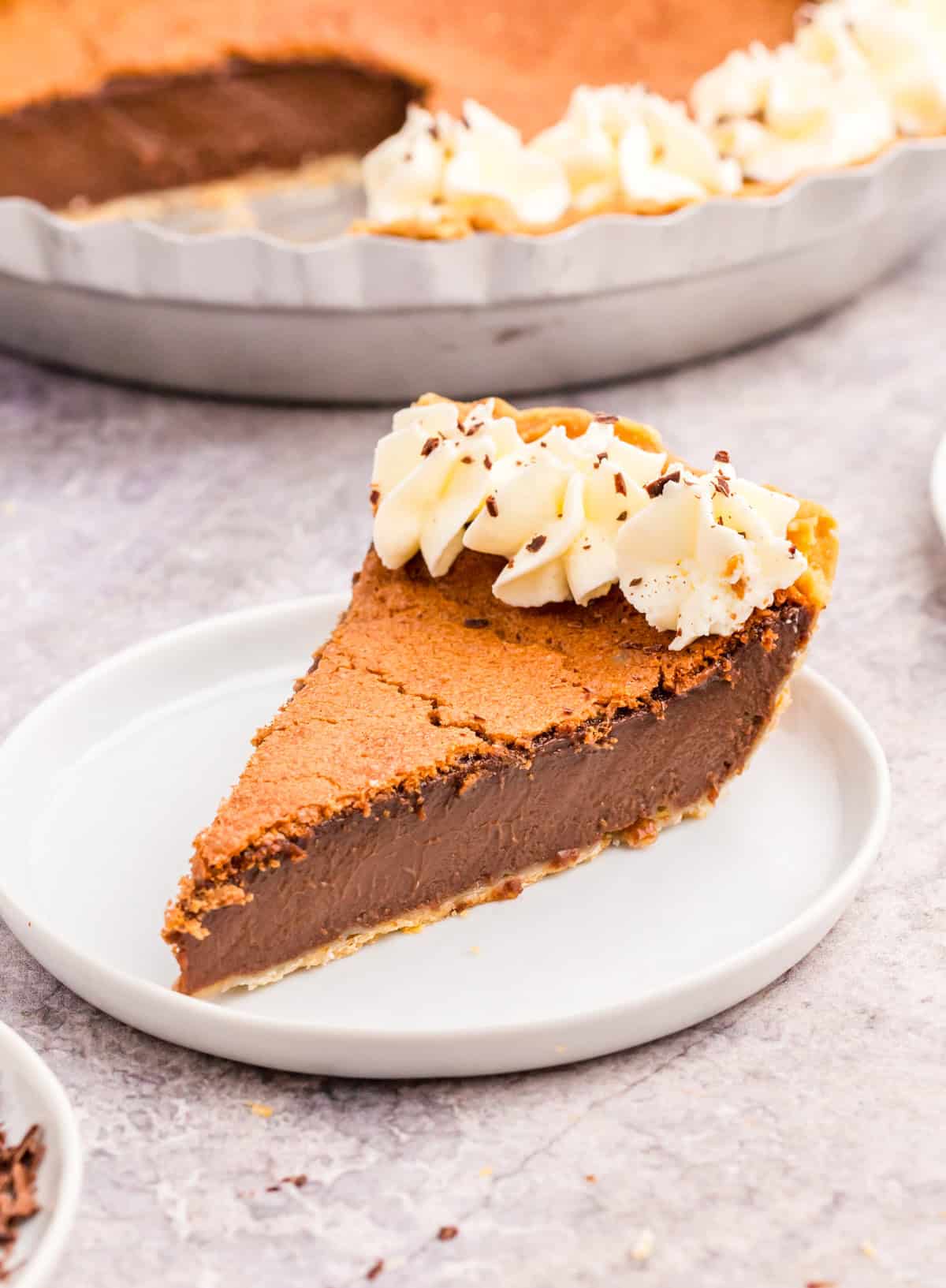 Slice of Fudge Pie on white plate with whipped cream and chocolate shavings.