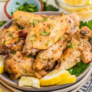 Close up square image of wings on plate topped with parsley and garnished with lemon wedges.