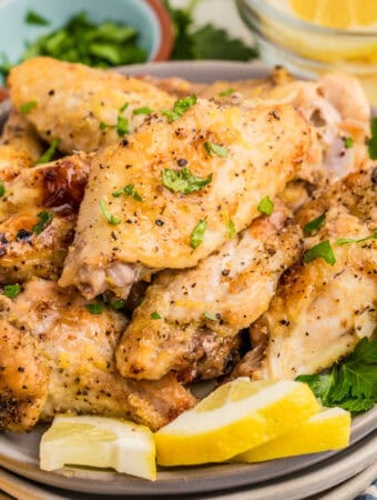 Close up square image of wings on plate topped with parsley and garnished with lemon wedges.