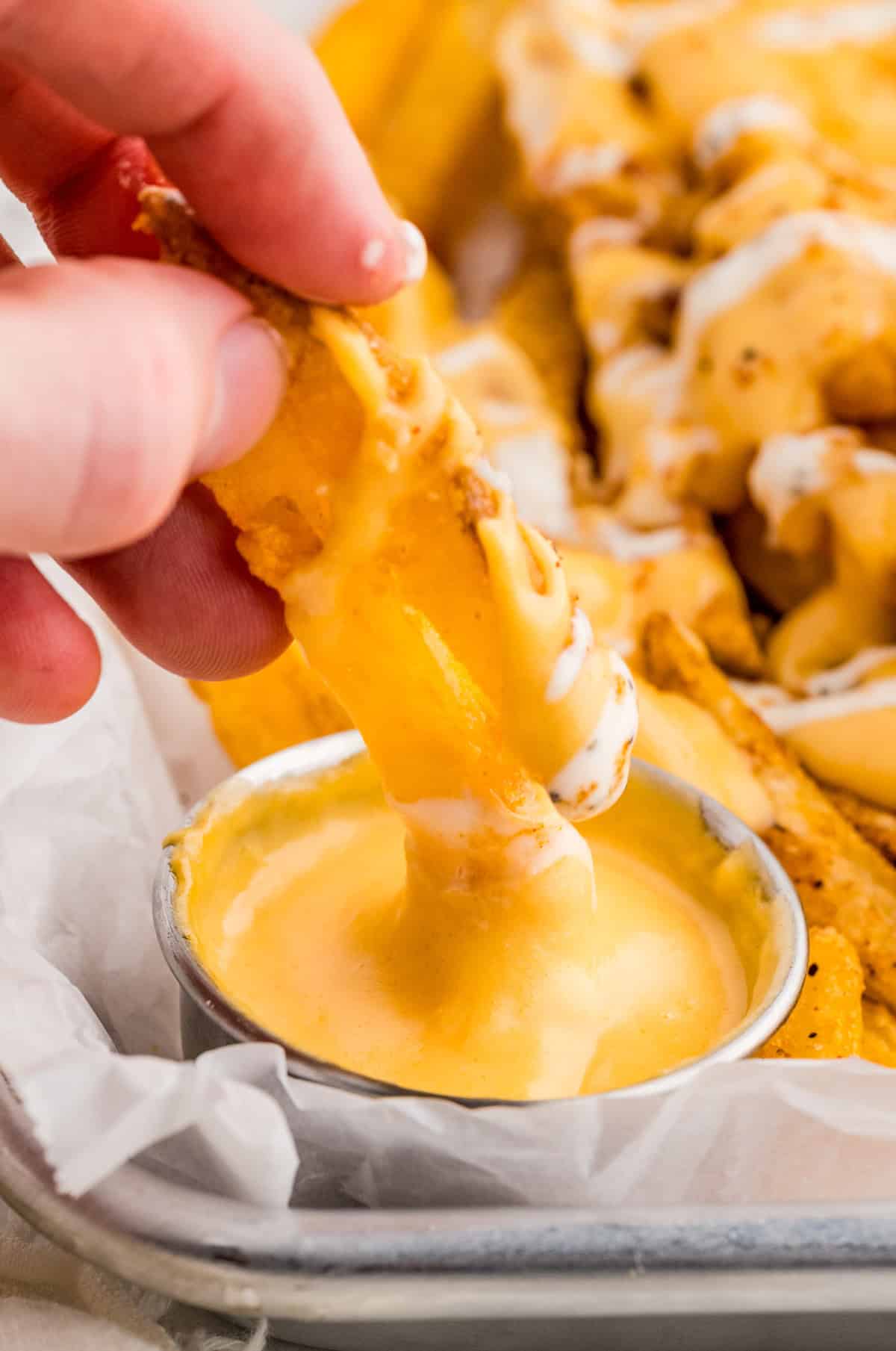 Hand dipping two fries into cheese sauce.