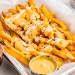 Close up of fries in a parchment lined pan with cheese sauce.