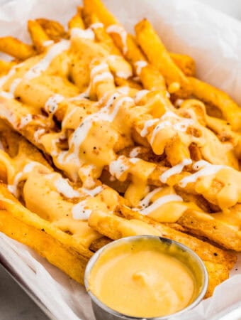 Close up of fries in a parchment lined pan with cheese sauce.