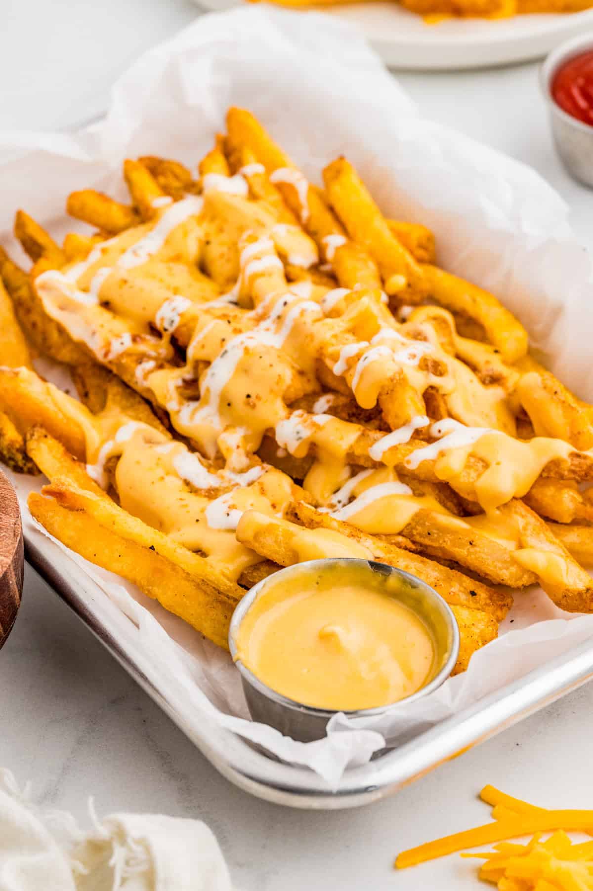 Louisiana Voodoo Fries on parchment lined pan with cheese sauce. Topped with cheese sauce, ranch and seasoning.