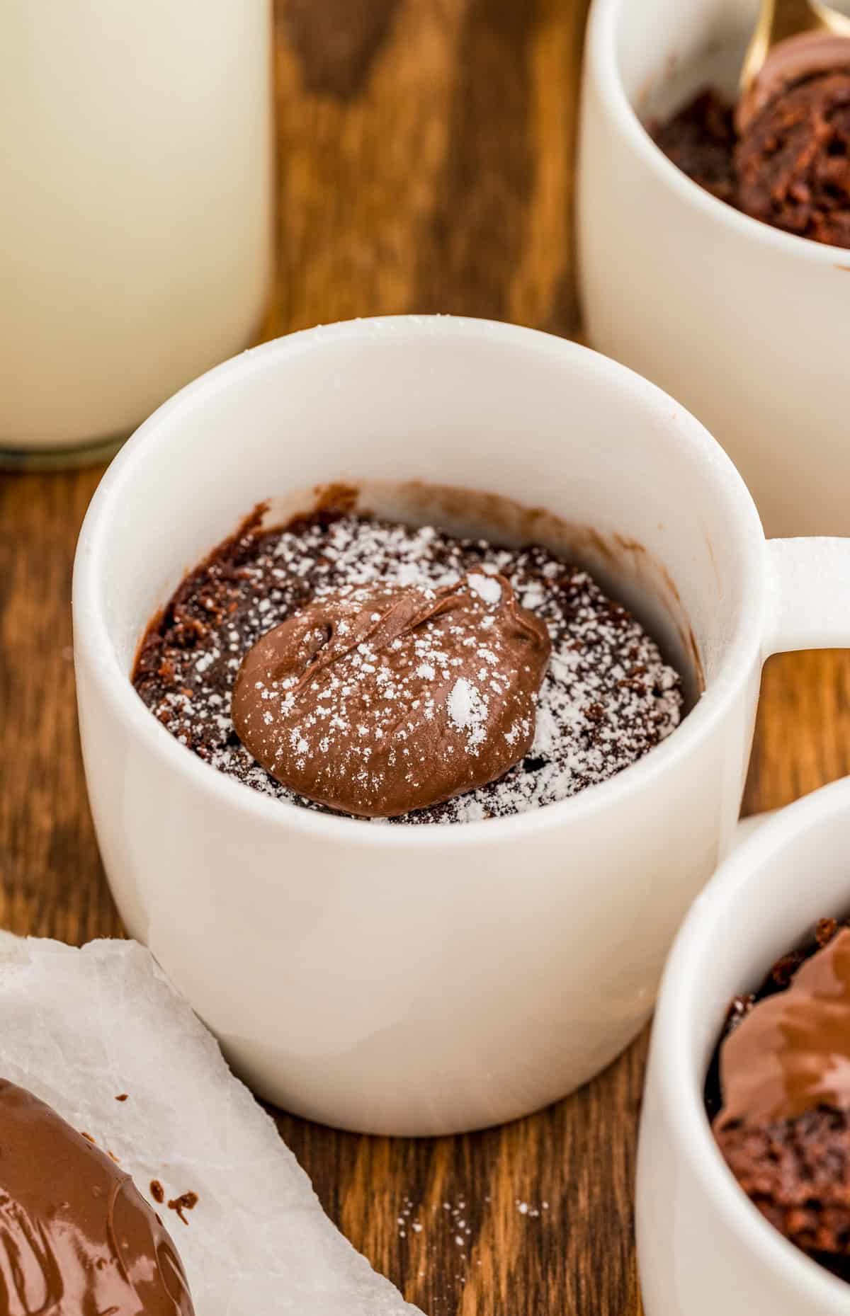 Finished Nutella Mug Cake in white mug topped with nutella and powdered sugar.