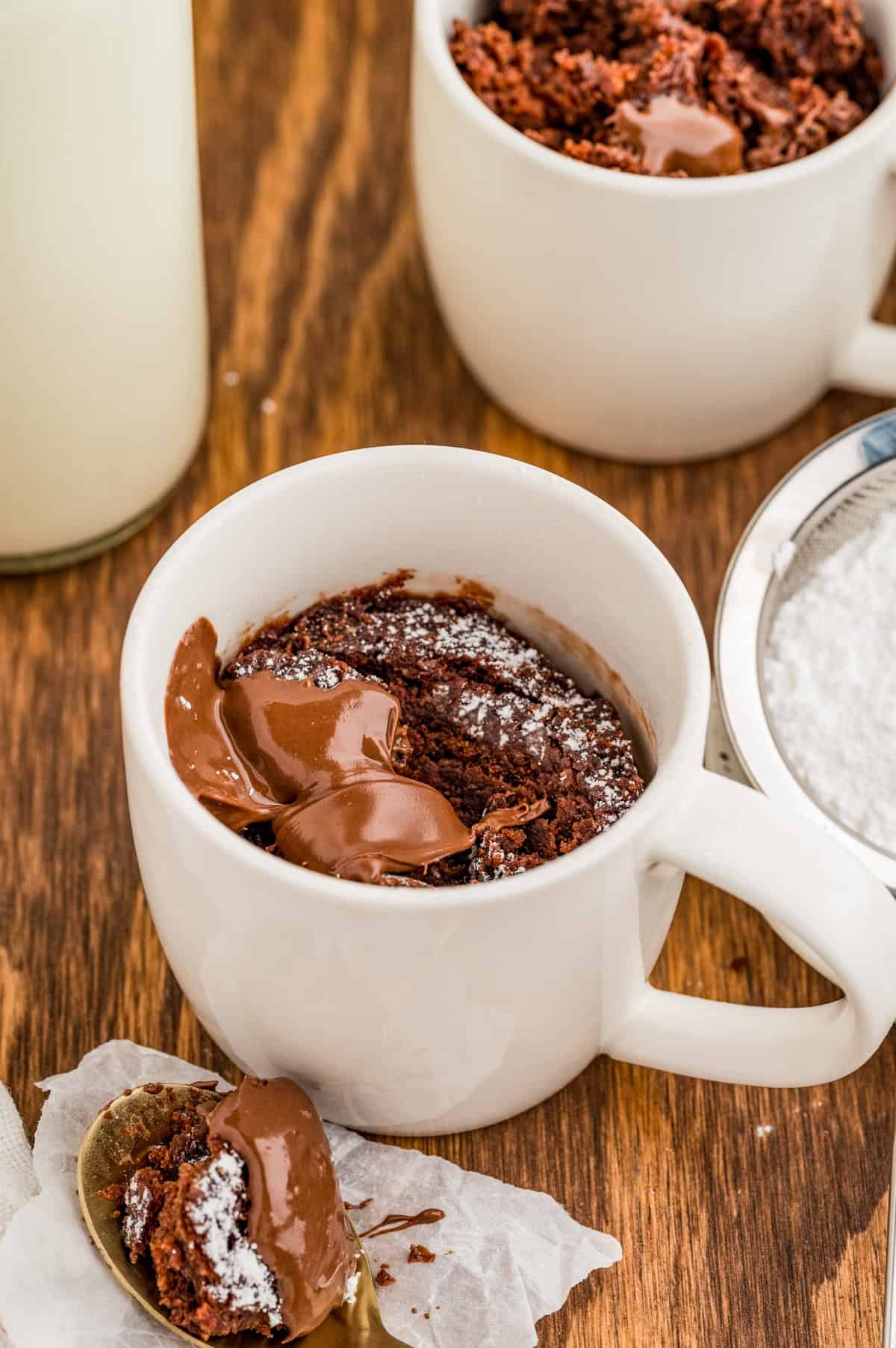 Finished cake with spoon next to mug with some cake on spoon.