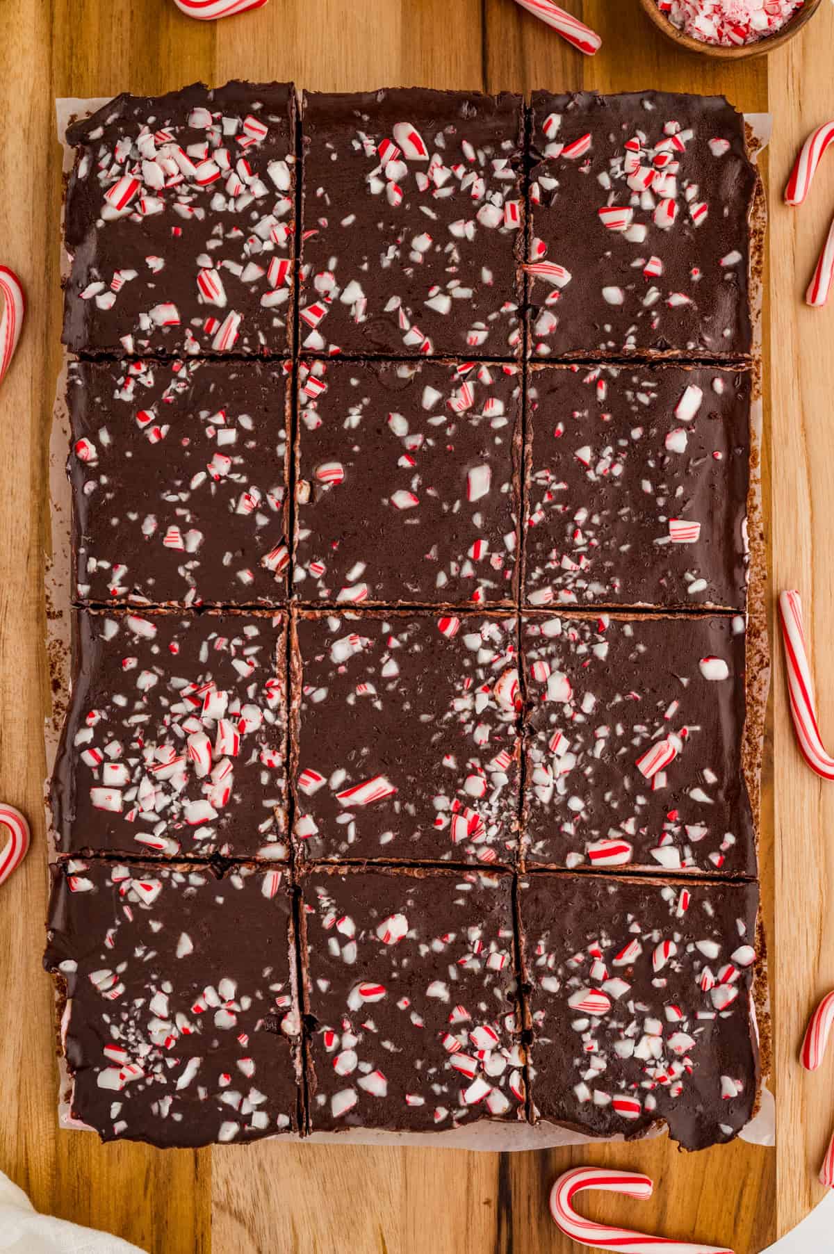 Overhead of brownies on wooden board cut into slices showing crushed candy canes on top.