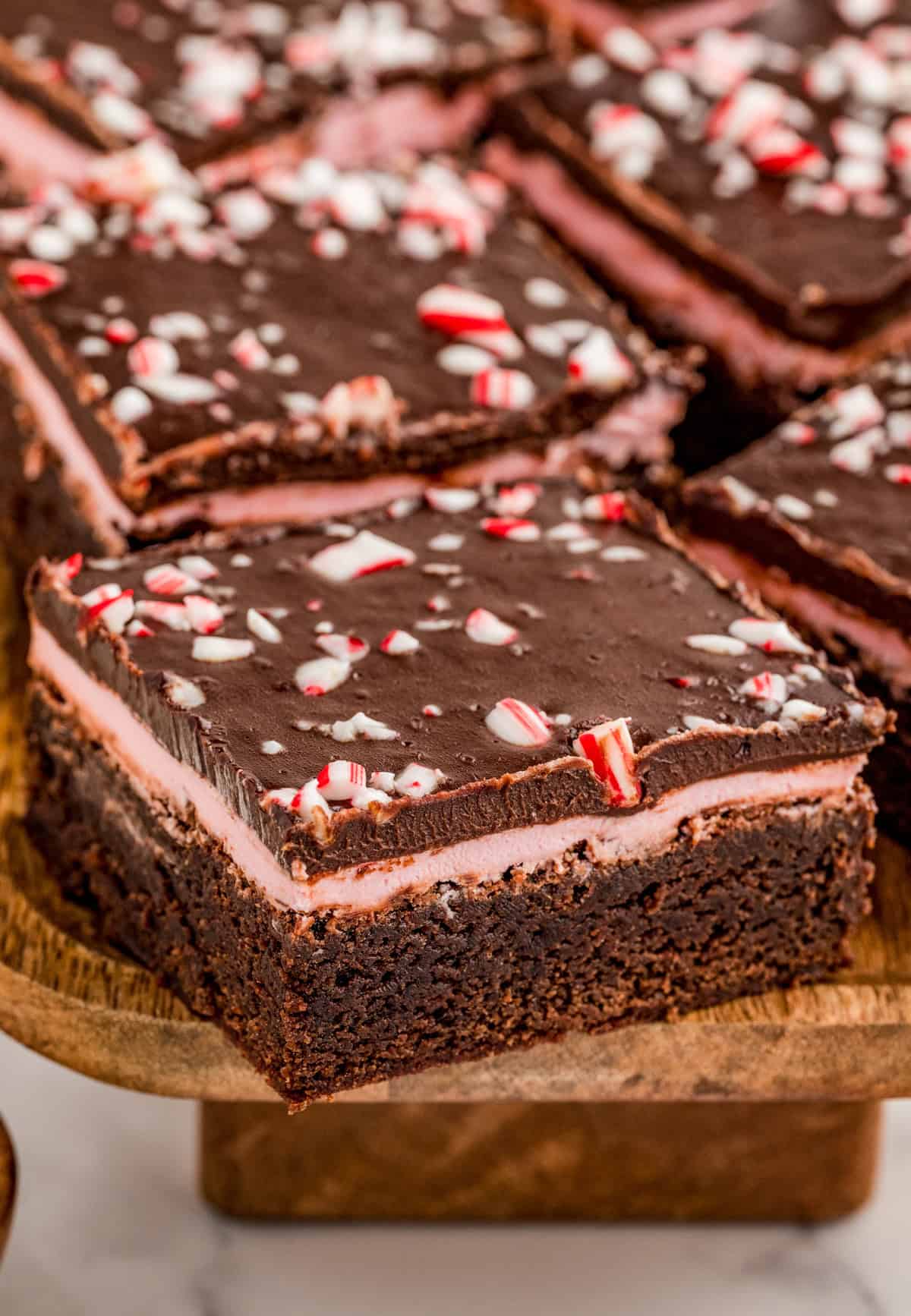 One of the Peppermint Brownies on wooden board showing the layers and the candy cane topping.