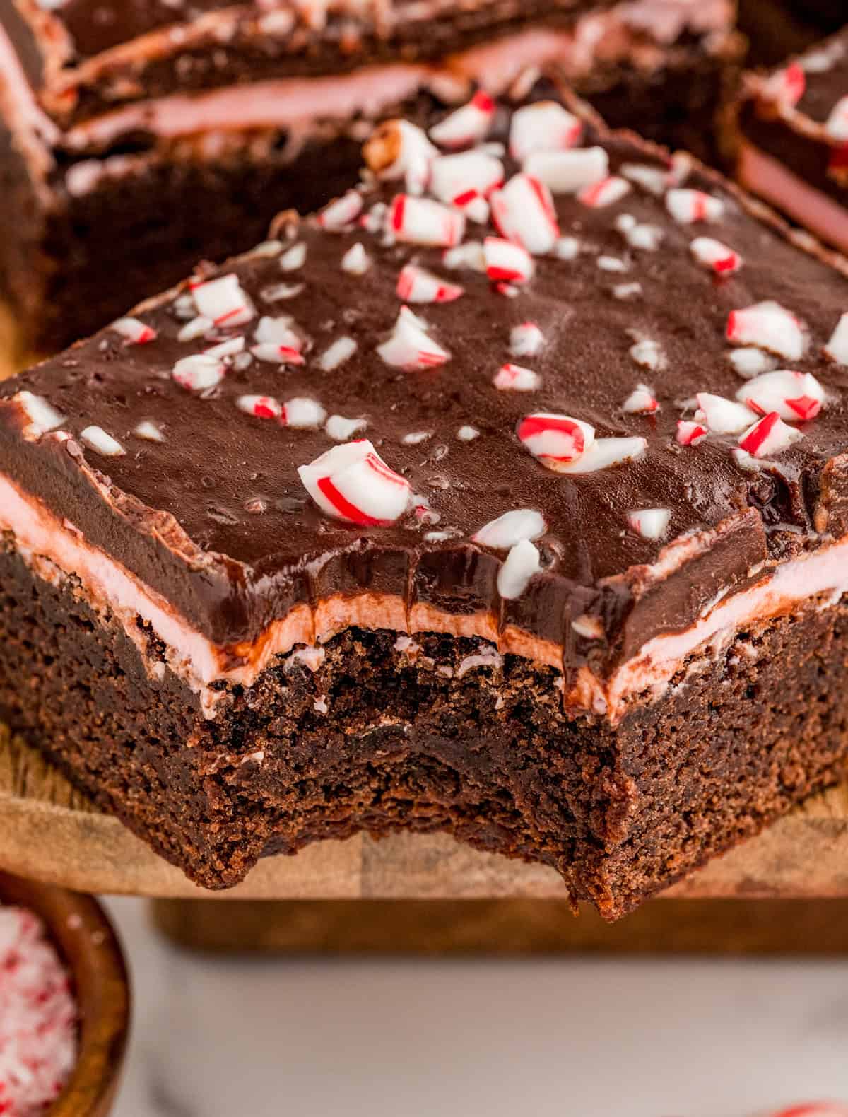 One brownie on wooden board with a bite taken out of it.