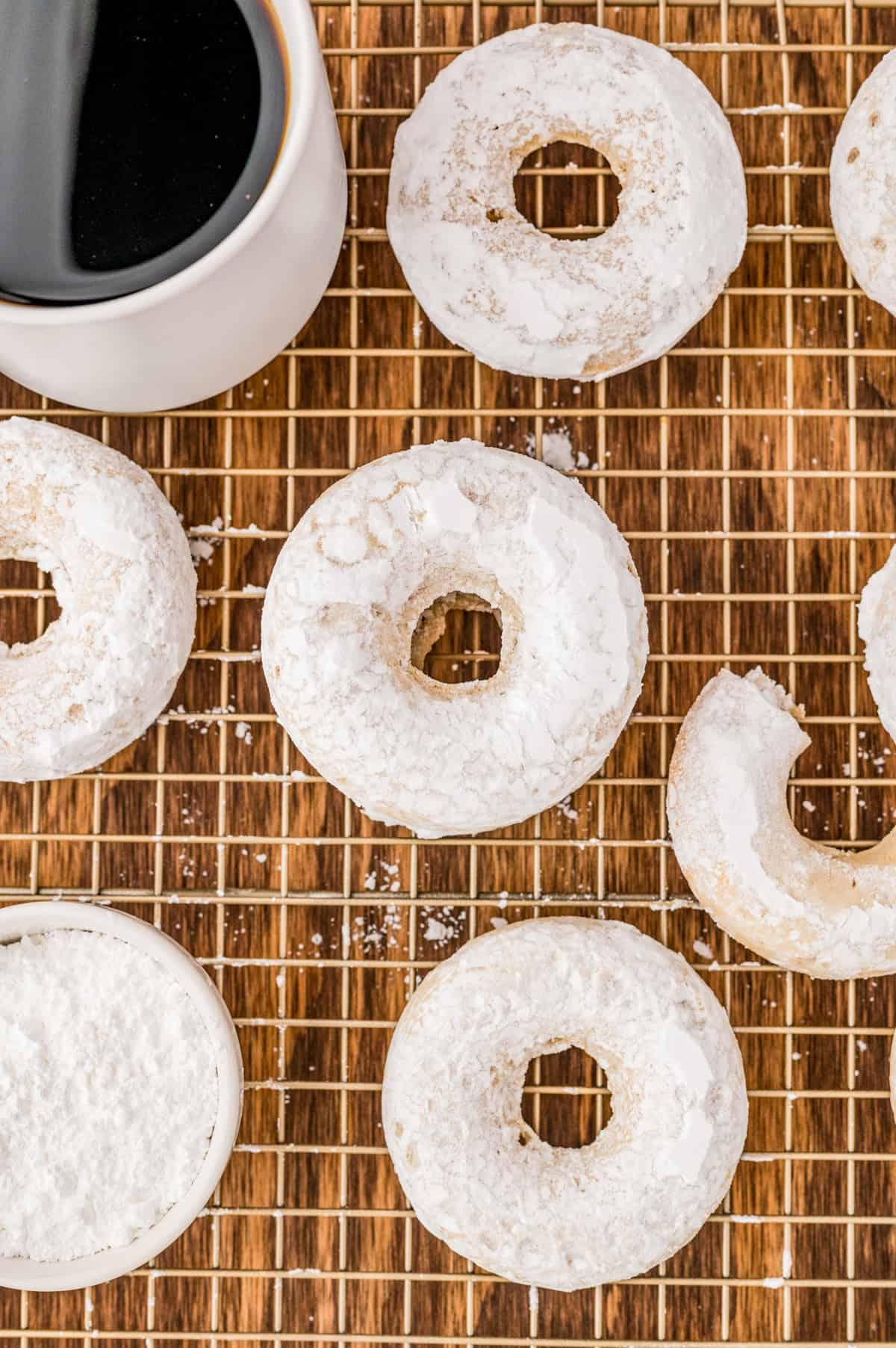 Overhead photo of finished donuts on wire rack with a cup of coffee.