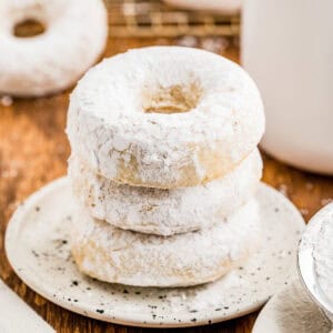 Square image of three stacked donuts on a white plate.