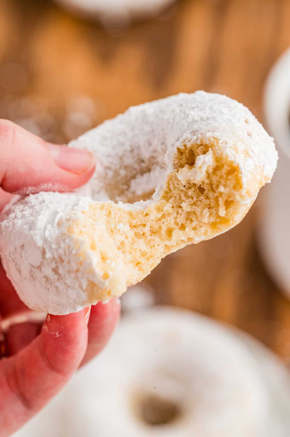 Hand holding up one of the donuts with a bite taken out of it.