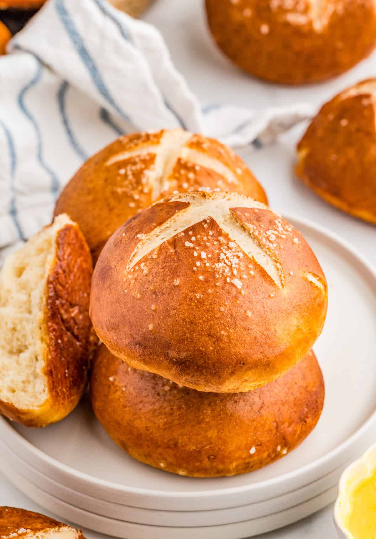 Stacked Pretzel Rolls on white plate with one torn in half.