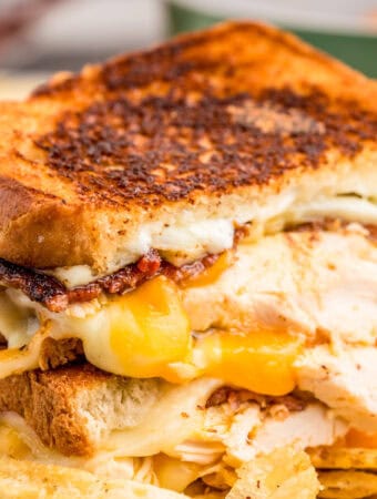 Close up square image of sandwich cut in half showing the melted cheese and other ingredients.