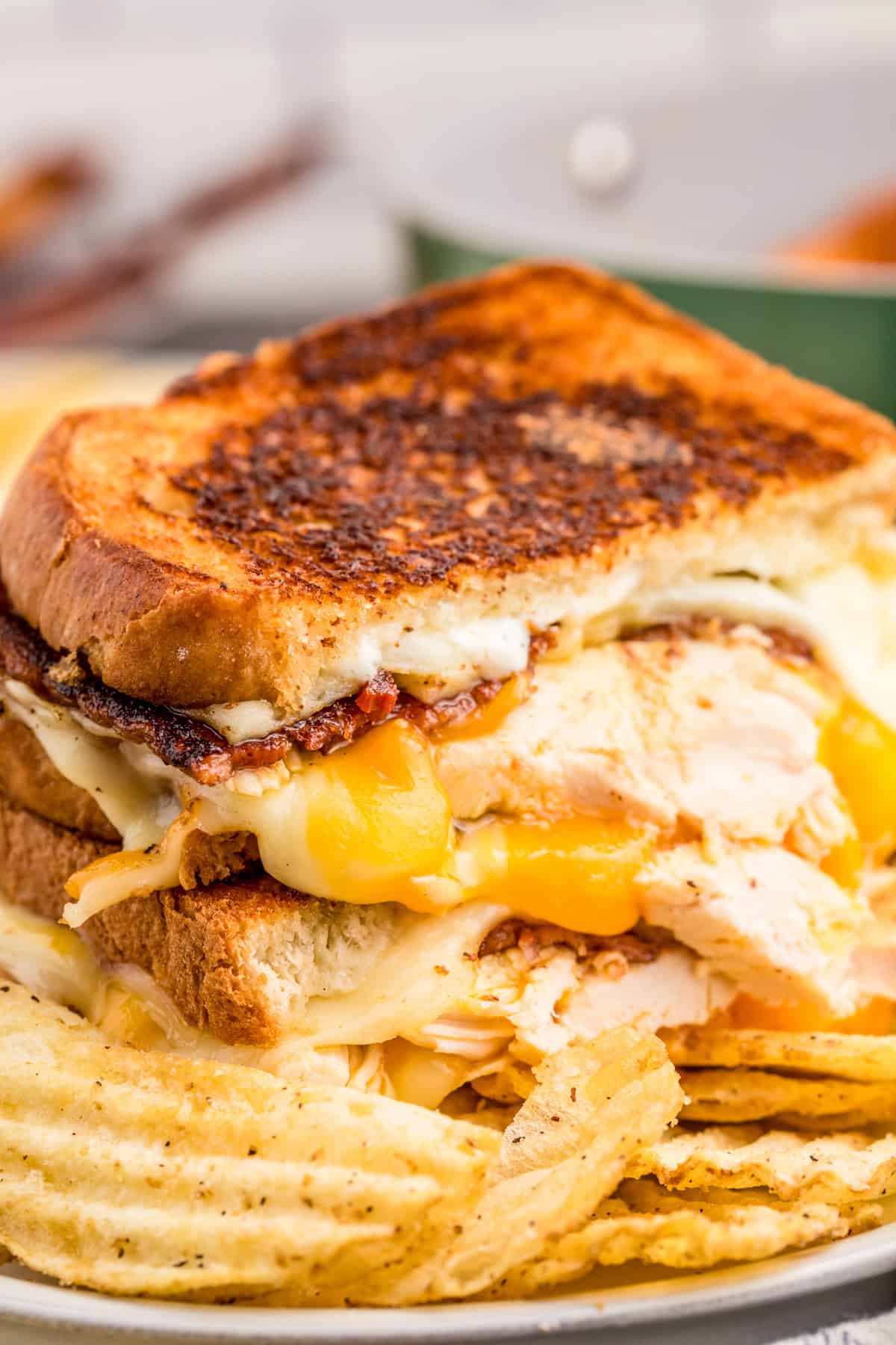 Chicken Bacon Ranch Grilled Cheese cut in half and stacked showing the melted cheese and other ingredients over a plate of chips.