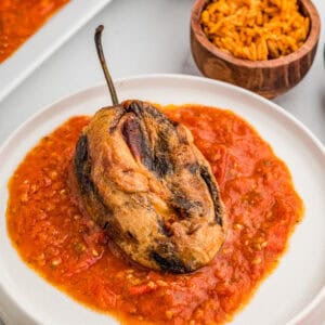 Square image of finished chile on white plate over sauce with mexican rice in background.