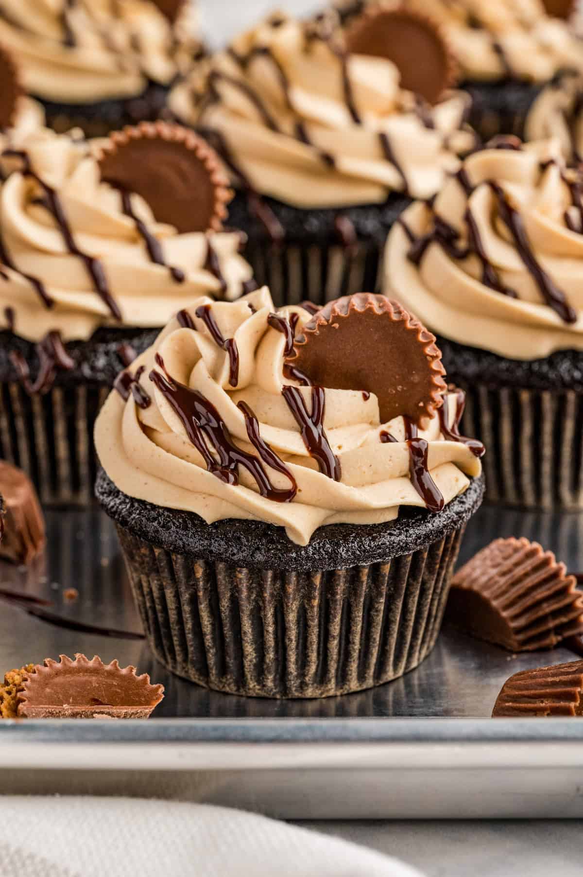 Finished Chocolate Peanut Butter Cupcakes on metal tray topped with frosting, ganache and mini Reese's.