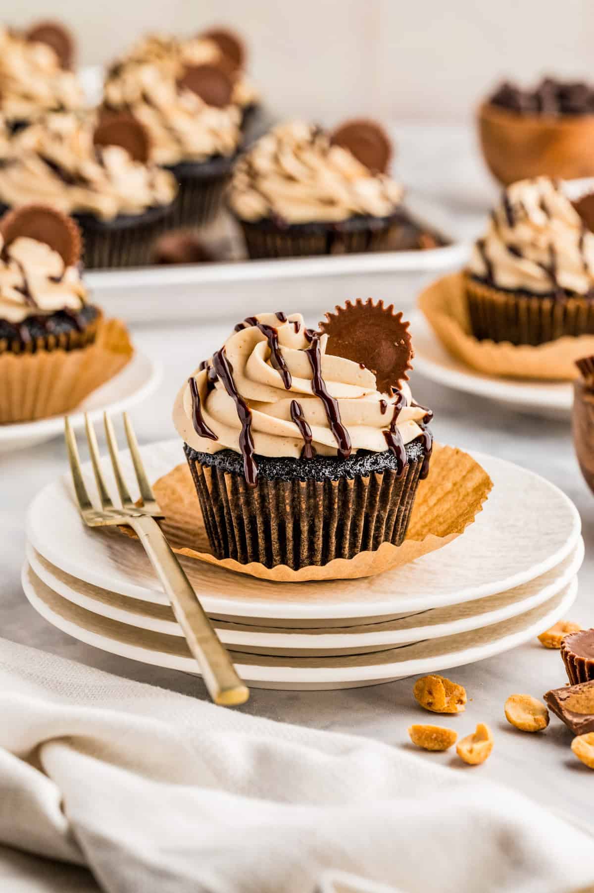 One cupcake on stacked white plates, garnished with cupcakes behind it.