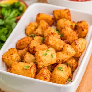 Close up square image of tots in white dish topped with parsley.