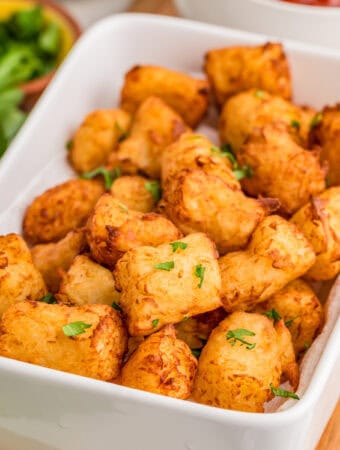 Close up square image of tots in white dish topped with parsley.