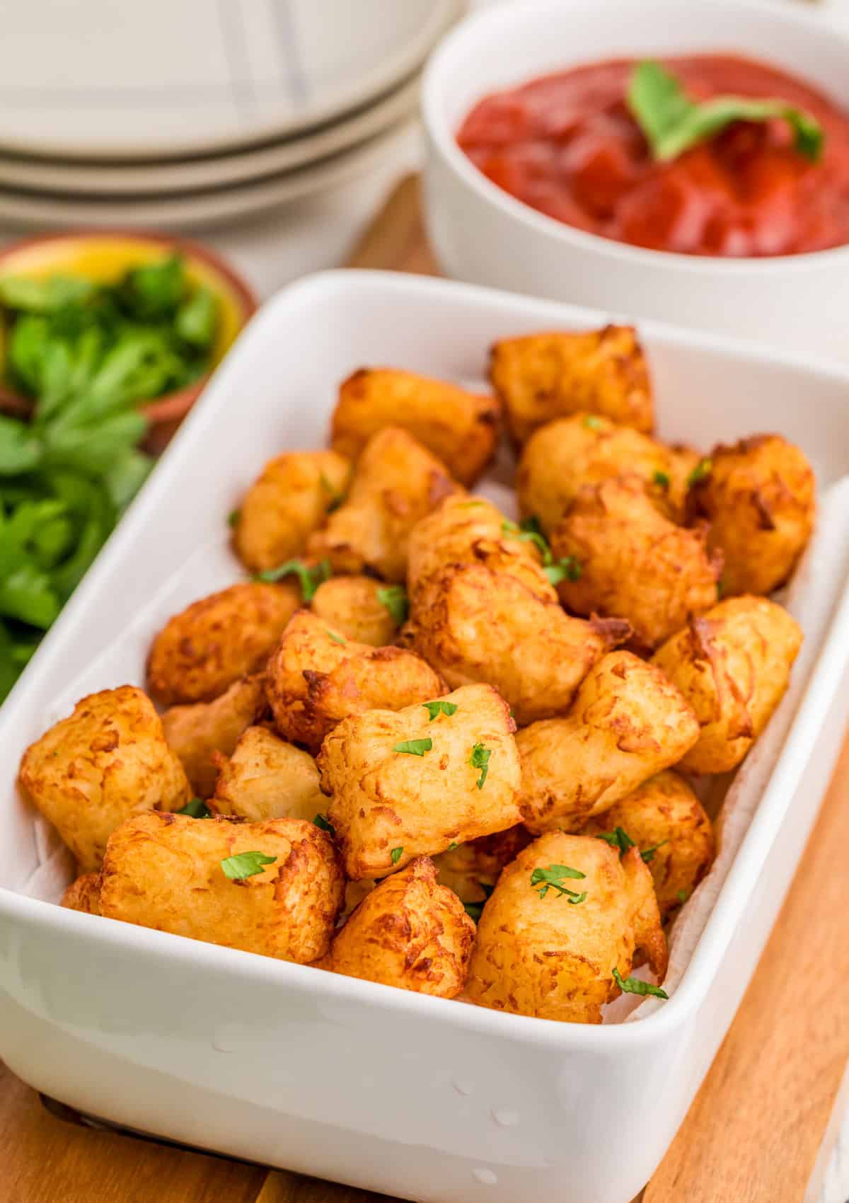 Homemade Tater Tots in white dish topped with parsley with ketchup in bowl in background.