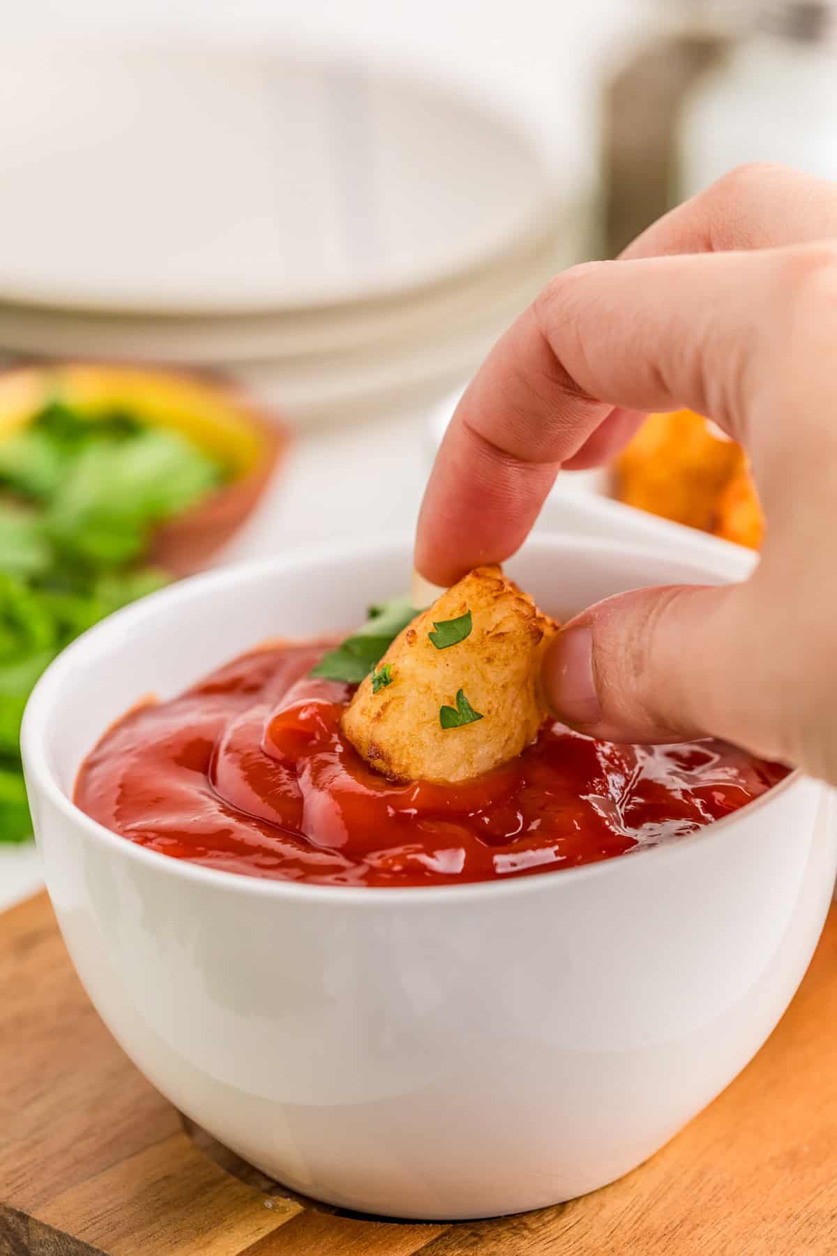 Hand dipping one of the tots into a bowl of ketchup.