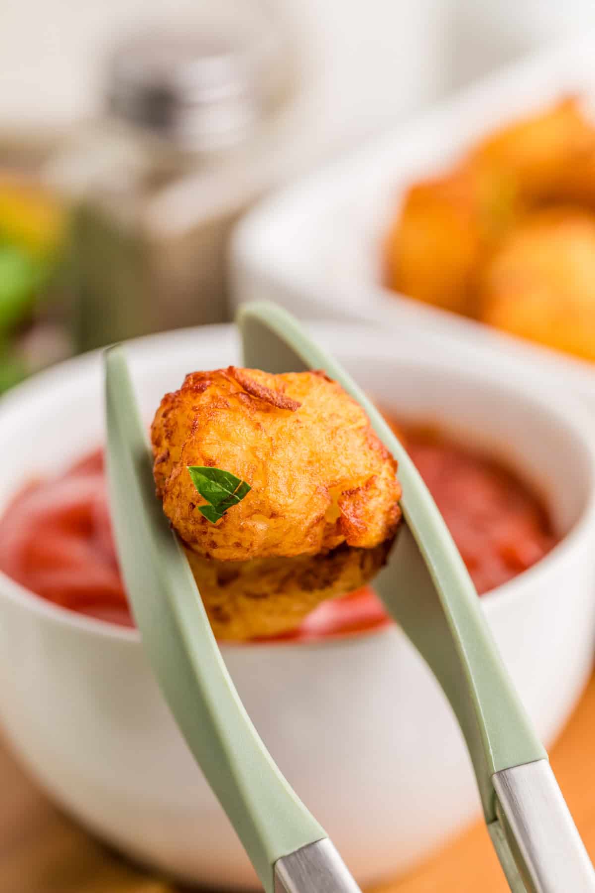 Tongs holding up some of the finished tots out of dish.