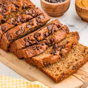 Square image of bread on wooden board cut in slices topped with chocolate chips.