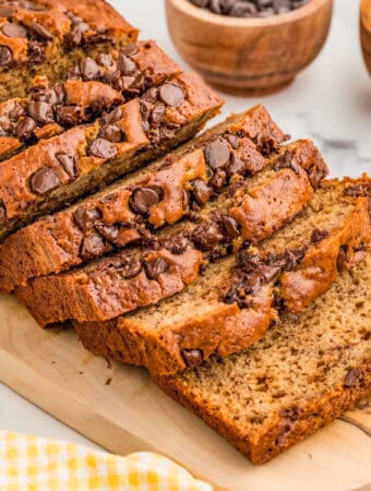 Square image of bread on wooden board cut in slices topped with chocolate chips.