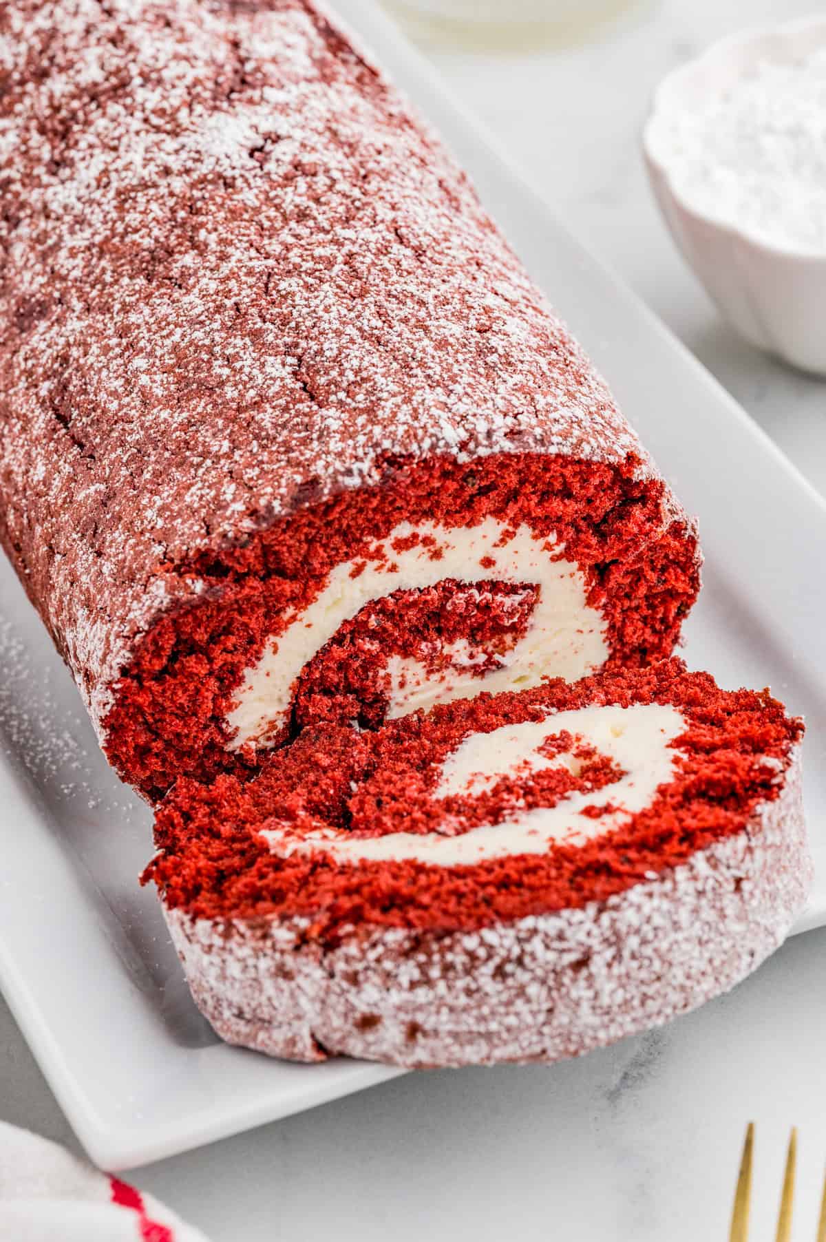 Cake roll on white serving plate with one slice cut showing the swirl of the cake.