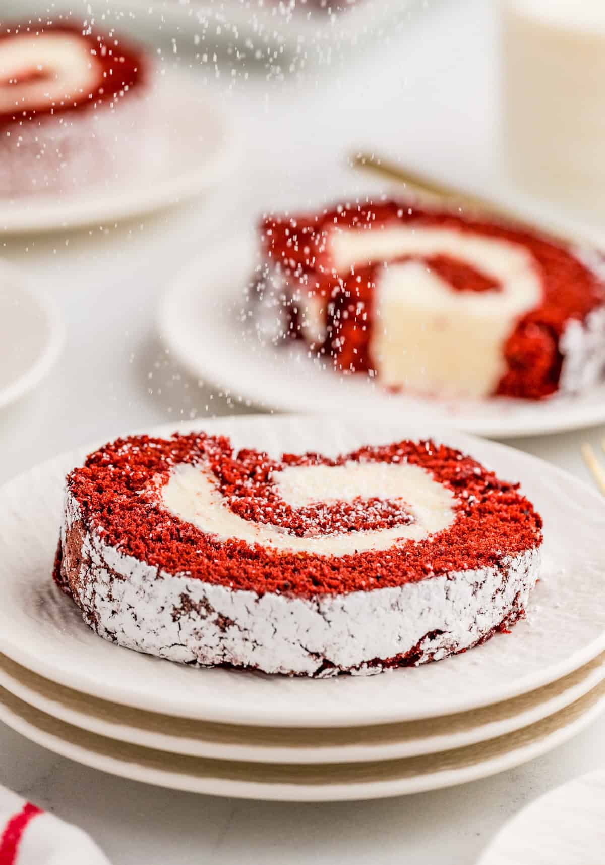 Slice of the Red Velvet Cake Roll on stacked white plates.