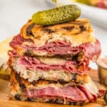 Close up image of sandwich cut in half and stacked on top of each other on wooden board.