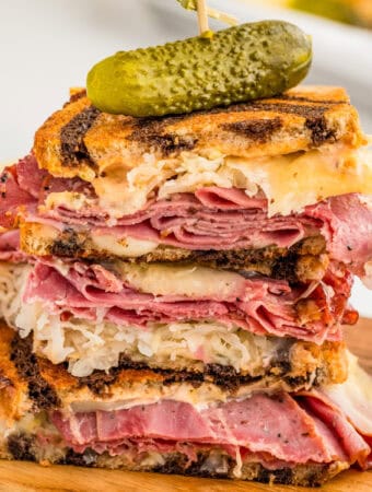 Close up image of sandwich cut in half and stacked on top of each other on wooden board.