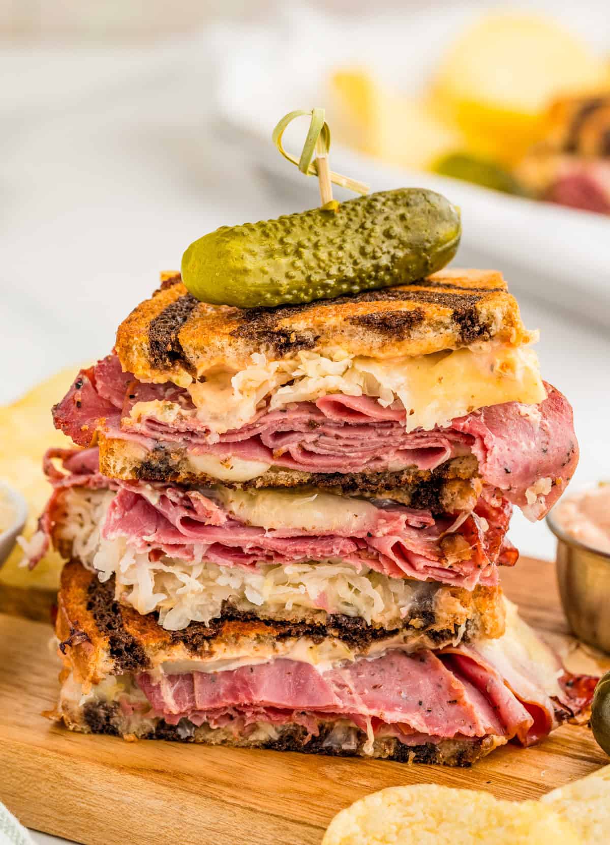 Reuben Sandwich Recipe cut in half stacked on top of one another on wooden board and topped with a pickle.