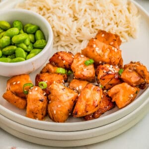 Close up square image of salmon on stacked plates with rice and edamame.